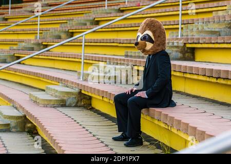 Homme d'affaires en costume noir avec masque de meerkat assis seul escaliers Banque D'Images