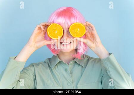 Jeune femme portant une perruque rose couvrant ses yeux avec des oranges Banque D'Images