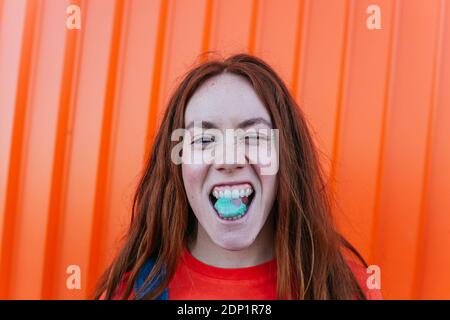 Jeune femme mâchant de la gomme tout en se tenant contre le mur orange Banque D'Images