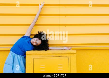 Portrait de la jeune femme afro-américaine avec des vêtements bleus et un fond de mur urbain jaune à Grenade, Espagne. Femme mur urbain afro-américain afro Banque D'Images