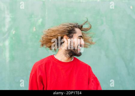 Un jeune homme barbu avec ses cheveux devant le mur vert Banque D'Images