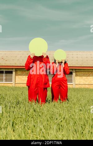 Jeune couple portant une combinaison rouge debout sur un champ caché faces derrière le cercle vert Banque D'Images