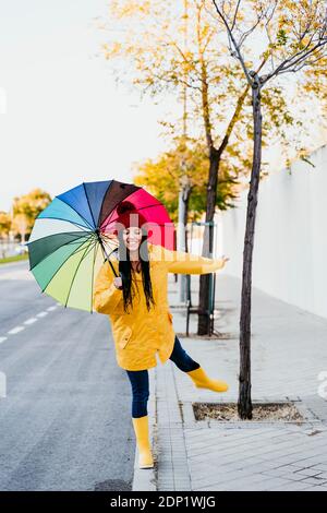 Femme avec une jambe relevée tenant un parapluie coloré debout sur le sentier Banque D'Images