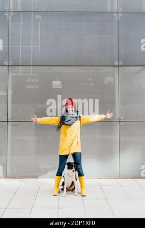 Une femme heureuse avec des bras tendus debout avec un chien sur le sentier contre l'extérieur du bâtiment Banque D'Images