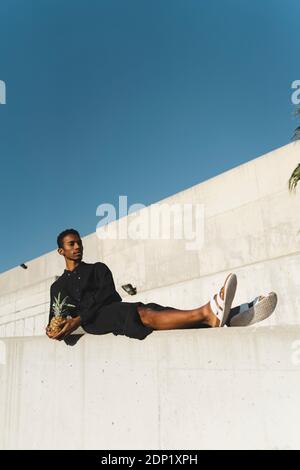 Jeune homme portant un caftan noir tenant un ananas Banque D'Images