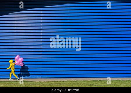 Petite fille avec des ballons roses portant un survêtement jaune marchant dans avant de l'arrière-plan bleu Banque D'Images