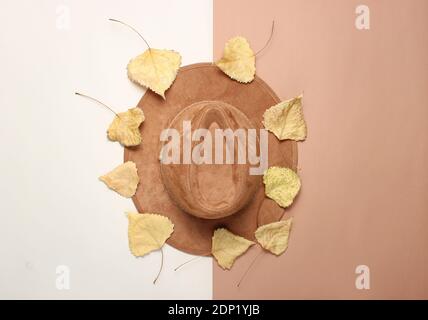 Chapeau feutre parmi les feuilles jaunes tombées sur fond de papier beige brun, minimalisme, fond créatif. Vue de dessus Banque D'Images