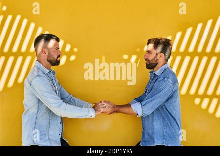 Couple gay tenant les mains tout en se tenant contre le mur jaune Banque D'Images