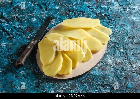 Tranches de pommes de terre sur une plate-forme en bois sur fond de béton bleu. Vue de dessus Banque D'Images