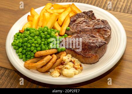 Steak Dinner - steak de bœuf, avec frites, petits pois, rondelles d'oignon et chou-fleur. Banque D'Images