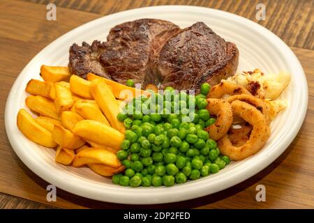 Steak Dinner - steak de bœuf, avec frites, petits pois, rondelles d'oignon et chou-fleur. Banque D'Images