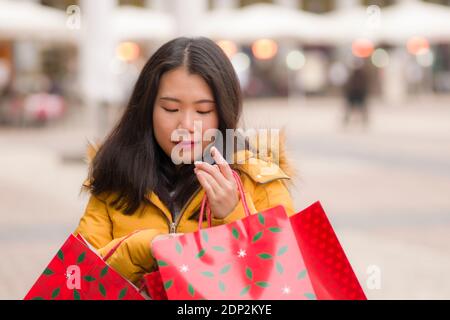 Fille asiatique appréciant le shopping de Noël - jeune heureux et beau Femme japonaise tenant un sac rouge à l'achat de cadeaux dans la rue marché de noël smili Banque D'Images