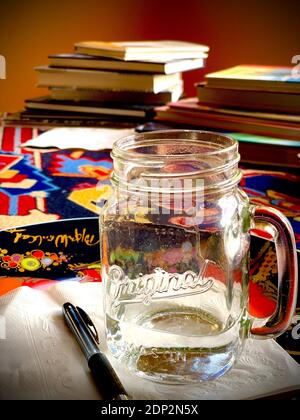 Pot en verre Mason original avec poignée sur matériau coloré et pile de livres en arrière-plan. Photo couleur, verticale, rétro-éclairée Banque D'Images