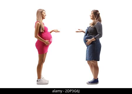 Photo de profil pleine longueur de deux femmes enceintes ayant un conversation et partage d'expériences isolées sur fond blanc Banque D'Images