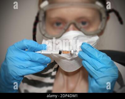 Jeune femme médecin portant un masque et des lunettes tenant vaccin covid-19 avec gants Banque D'Images