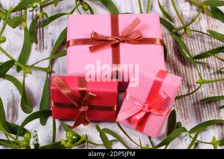 Enveloppé rouge et rose cadeaux de Noël ou d'autres célébration et branche de gui vert sur fond de bois vieux Banque D'Images