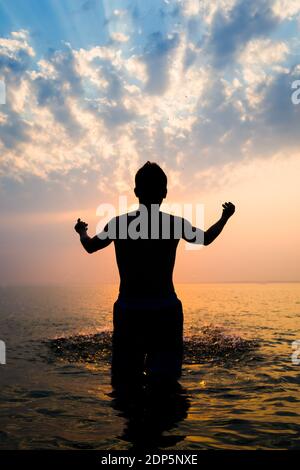 Silhouette d'homme avec des éclaboussures dans l'eau au coucher du soleil Arrière-plan Banque D'Images