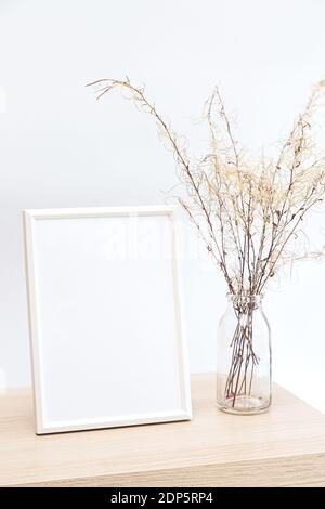 Maquette d'un cadre photo blanc dans un style minimaliste intérieur avec un bouquet d'herbe de pampas dans un verre vase sur fond de mur blanc Banque D'Images