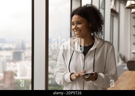 Femme biraciale souriante utiliser le téléphone portable regarder dans le rêve à distance Banque D'Images