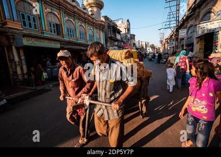 Jamnagar, Gujarat, Inde - décembre 2018 : ouvriers indiens transportant des marchandises sur chariot à roues dans les rues marchandes de la vieille ville de Jamnagar. Banque D'Images