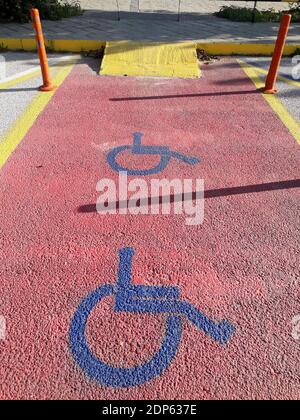 Panneau jaune pour personnes handicapées marquant une place dans un parking, sur fond rouge dans une marina en Grèce Banque D'Images