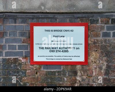 Un panneau réseau ferroviaire sous un pont ferroviaire avec un numéro de téléphone à appeler en cas de collision d'un véhicule routier avec le pont. Banque D'Images