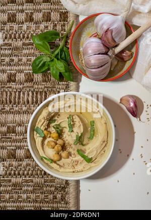 Bol avec houmous crémeux fraîchement confectionnés, avec pois chiches, basilic et ail isolés sur fond coloré Banque D'Images