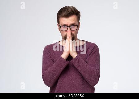 Jeune prière concentrée dans les lunettes espérant pour tous les meilleurs, demandant la santé, bonne chance, aide. Prise de vue en studio Banque D'Images
