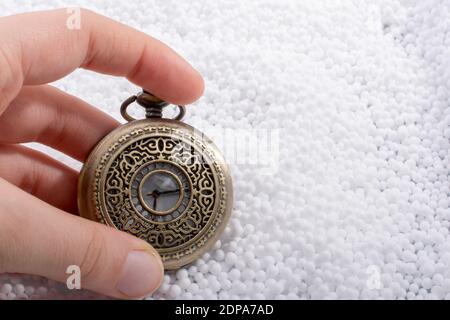 Image rognée de la main tenant une montre de poche antique sur des perles en polystyrène