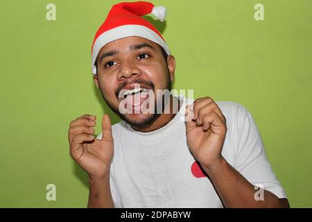 Homme avec chapeau de noël surpris et exprimant des émotions, célébration de Noël sur fond vert, mise au point sélective avec flou. Banque D'Images