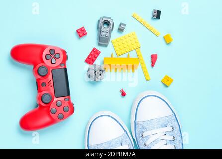 Chaussures et jouets des années 80 sur fond bleu. Manette de jeu rouge, briques constructeur pour enfants, baskets, vue de dessus Banque D'Images