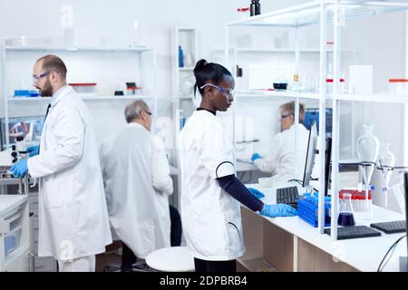 Un scientifique africain et ses collègues font des expériences en laboratoire stérile. Une équipe multiethnique de chercheurs travaillant dans une solution de test en laboratoire de microbiologie à usage médical. Banque D'Images