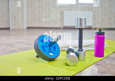 AB Wheel, haltères, une bouteille d'eau sur tapis de gymnastique dans le hall. Concept de formation Banque D'Images