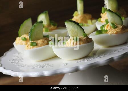 Oeufs farcis épicés garnie avec le concombre et le poireau sur plaque blanche. Fond rustique en bois Banque D'Images