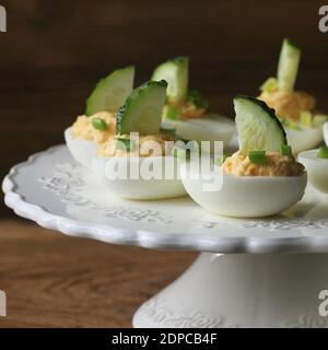 Oeufs farcis épicés garnie avec le concombre et le poireau sur plaque blanche. Fond rustique en bois Banque D'Images
