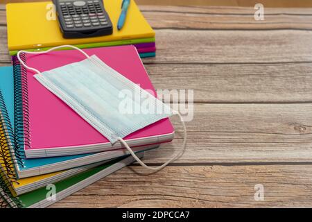 A selective focus shot of notebooks, sanitary mask, pencils, calculator on a wooden table Banque D'Images