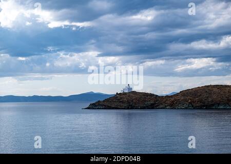 Grèce, île de Kea Tzia. Phare blanc sur un cap rocailleux, ciel bleu nuageux et fond d'eau de mer sombre et coloré. Été, destination touristique Banque D'Images