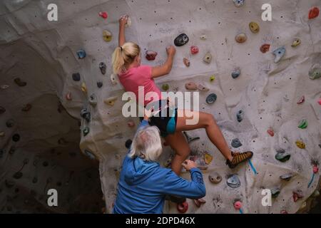 Instructeur d'escalade assistant une jeune femme blonde étudiant pendant l'escalade dans un mur d'escalade. Processus d'apprentissage. Banque D'Images