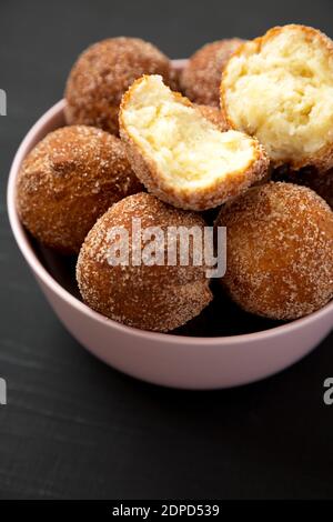 Trous de beignets faits maison dans un bol rose sur une surface noire, vue latérale. Banque D'Images