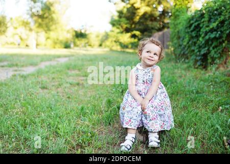 Petite fille souriante dans une jolie robe assise sur la souche et la recherche Banque D'Images