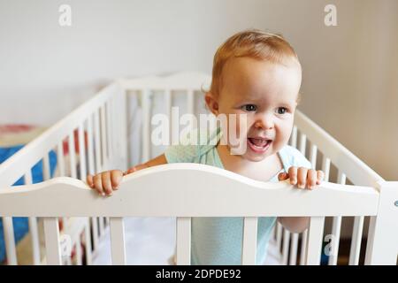Magnifique bébé debout dans un berceau. Portrait d'une petite fille adorable dans un berceau et rire Banque D'Images