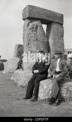 Années 1950, historique, Stonehenge, le célèbre momument préhistorique sur la plaine de Salisbury dans le Wiltshire, Angleterre, Royaume-Uni. À cette époque, les visiteurs pouvaient marcher librement parmi les anciennes pierres de sarsen et s'asseoir sur elles - comme peuvent le voir les deux hommes ici - sans aucun problème, quelque chose qui plus tard ne serait pas autorisé. Banque D'Images