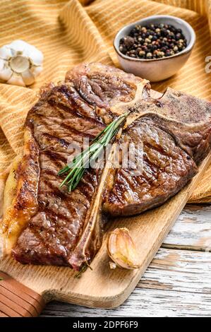 Steak d'os grillé sur une planche à découper. Bœuf en os cuit. Fond en bois blanc. Vue de dessus. Banque D'Images