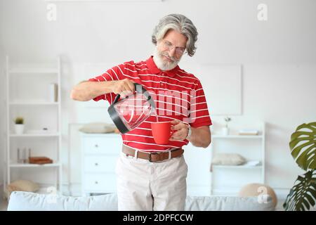 Homme mûr versant de l'eau chaude de la bouilloire électrique dans la tasse à la maison Banque D'Images