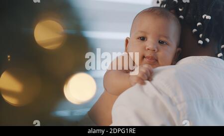 Beau nouveau-né Mulatto bébé appréciant les hugs de son père noir près de l'arbre de noël. Vacances en famille multiraciale. Photo de haute qualité Banque D'Images