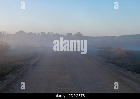 Brouillard traversant une route de terre par un lac tandis que le soleil se lève sur un matin d'automne frais. Banque D'Images