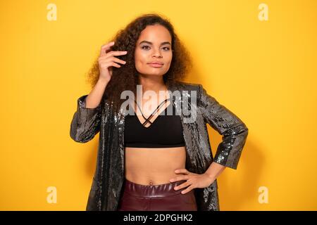 Posh beauté ethnique modèle fille avec belle coiffure sourire regardant l'appareil photo portant blouson noir brillant. Bonne jeune fille fixant les cheveux debout Banque D'Images