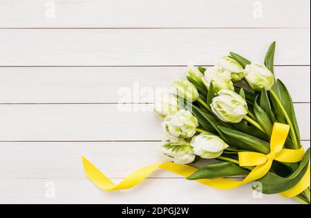 Bouquet de tulipes blanches décorées d'un ruban jaune sur fond de bois blanc.Vue de dessus, espace de copie Banque D'Images