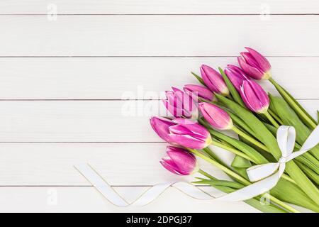 Bouquet de tulipes rose vif avec ruban blanc sur fond blanc en bois. Vue de dessus, espace de copie Banque D'Images