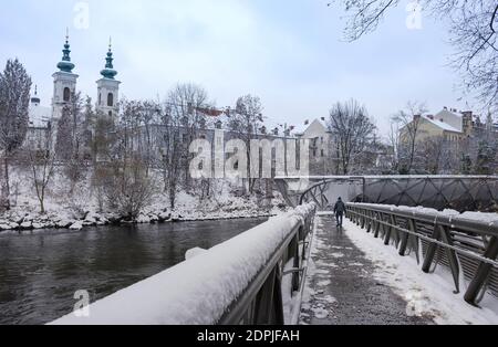 Pont Murinsel sur la rivière Mur et l'église Mariahilfer en arrière-plan, à Graz, en Styrie, en Autriche, avec de la neige, en hiver Banque D'Images